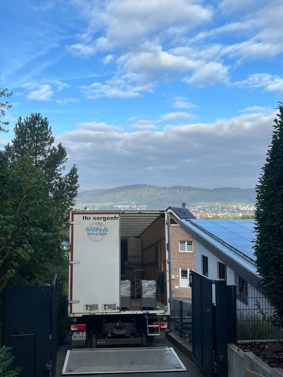 Heck des MINA-Umzüge-LKW mit offener Ladebordwand am Hoftor in Bad Driburg, im Hintergrund der Blick ins Tal